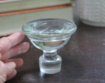 May include: A clear glass pedestal bowl with a rounded top and a short, cylindrical base. The bowl is filled with liquid, reflecting the surrounding environment. The design is simple and elegant, suitable for serving small portions.