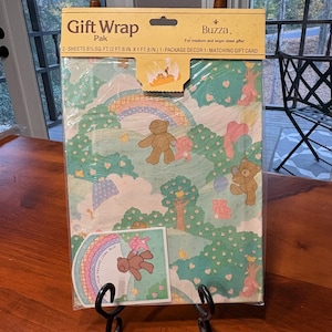 Könnte beinhalten: Geschenkpapier-Paket mit einem skurrilen Design mit Teddybären, Regenbogen und Herzen. Das Paket enthält zwei Bögen, eine passende Geschenkkarte und den Text "YOUR DREAMS COME TRUE". Das Papier ist 76 cm x 51 cm groß.