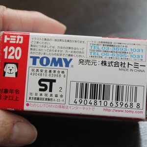 Pode incluir: Uma caixa de brinquedos Tomy vermelha e branca com texto japon&ecirc;s e um logotipo de cachorro. A caixa exibe o n&uacute;mero 120 e o texto "Made in China". A caixa &eacute; segurada por uma m&atilde;o.