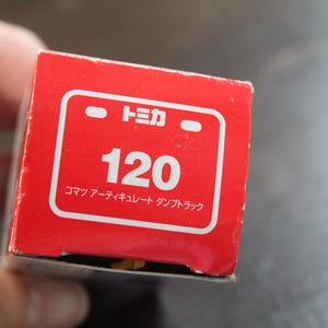 Pode incluir: Uma caixa vermelha com texto e gr&aacute;ficos brancos. O texto inclui o n&uacute;mero "120" e caracteres japoneses. A caixa &eacute; para um ve&iacute;culo de brinquedo, provavelmente um cami&atilde;o basculante.