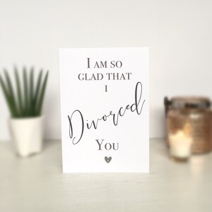 May include: A white card with the text "I am so glad that I divorced you" in black cursive font. A small silver heart is below the text.