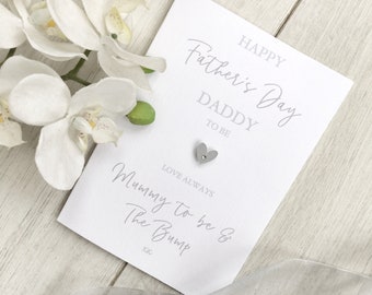 May include: A white card with the text "Happy Father's Day Daddy to be Love Always Mummy to be & The Bump xx" in grey script. A small silver heart is attached to the card.