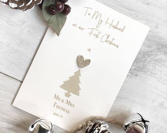 May include: A white card with gold lettering that reads "To My Husband on our First Christmas as Mr. & Mrs. Thomas 2017". A gold glitter heart is on top of a gold glitter Christmas tree.