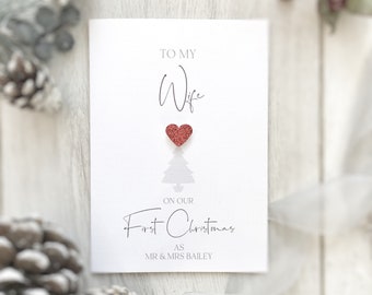 May include: A white card with the text "To my Wife" and a red glitter heart. Below the heart is a gray silhouette of a Christmas tree. The text "On our First Christmas as Mr. & Mrs. Bailey" is printed below the tree.