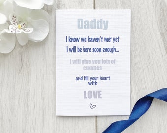 May include: A white card with blue text that reads "Daddy I know we haven't met yet I will be here soon enough... I will give you lots of cuddles and fill your heart with LOVE".