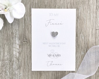 May include: White card with the text "To my fiancé" and a silver glitter heart. Below the heart is the text "Next Valentine's Day we will be Mr & Mrs Thomas".