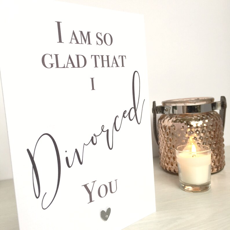 May include: White card with the text "I am so glad that I divorced you" in black lettering. The word "divorced" is written in cursive. A small silver heart is attached to the bottom of the card.