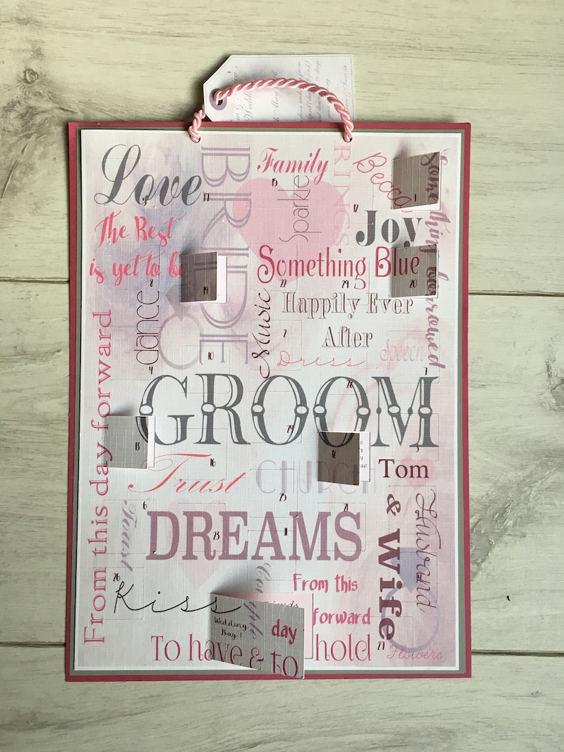 May include: A pink and white card with the word "GROOM" in large letters. The card has a variety of other words and phrases printed on it, including "Love", "Family", "Something Blue", "Happily Ever After", "Trust", "Dreams", "Kiss", "To Have & To Hold", and "Wedding Day".