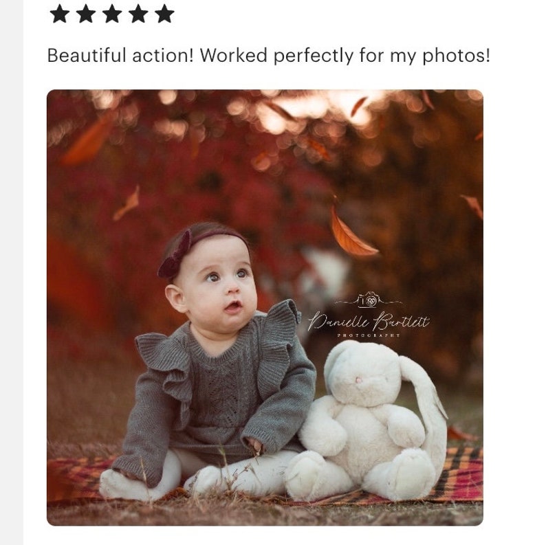 May include: A baby girl wearing a gray sweater with ruffles sits on a plaid blanket with a white stuffed bunny. The background is a blurred image of fall foliage.