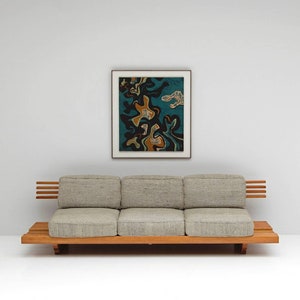 May include: A light gray three-seater sofa with a wooden frame and slatted back and arms. The sofa is positioned in front of a white wall with a framed abstract painting featuring black, blue, and orange shapes.