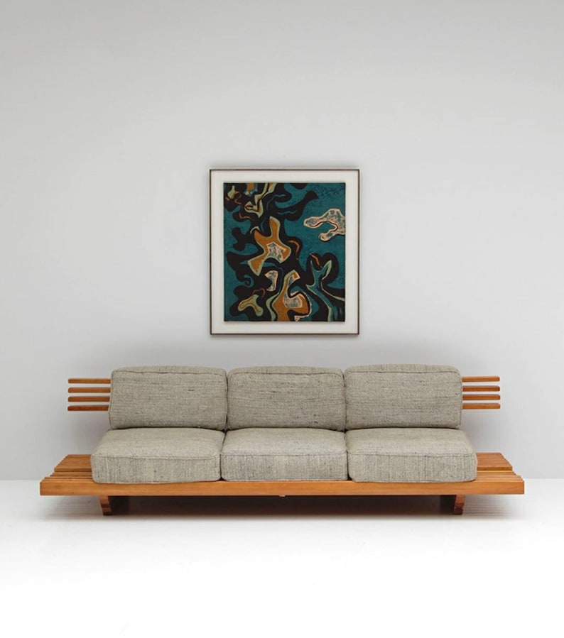 May include: A light gray three-seater sofa with a wooden frame and slatted back and arms. The sofa is positioned in front of a white wall with a framed abstract painting featuring black, blue, and orange shapes.