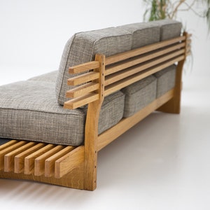 May include: A gray fabric sofa with a wooden frame and slatted back. The sofa has a simple, modern design and is perfect for a living room or den.