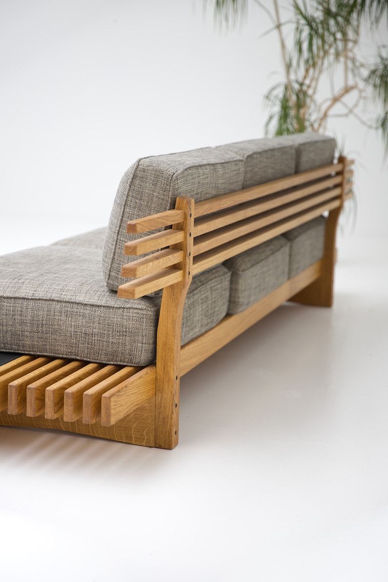 May include: A gray fabric sofa with a wooden frame and slatted back. The sofa has a simple, modern design and is perfect for a living room or den.