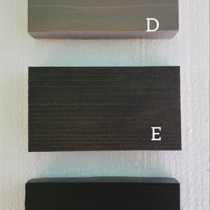 May include: Three wood samples, labeled D, E, and F. The top sample is a light gray wood, the middle sample is a dark gray wood, and the bottom sample is a black wood.