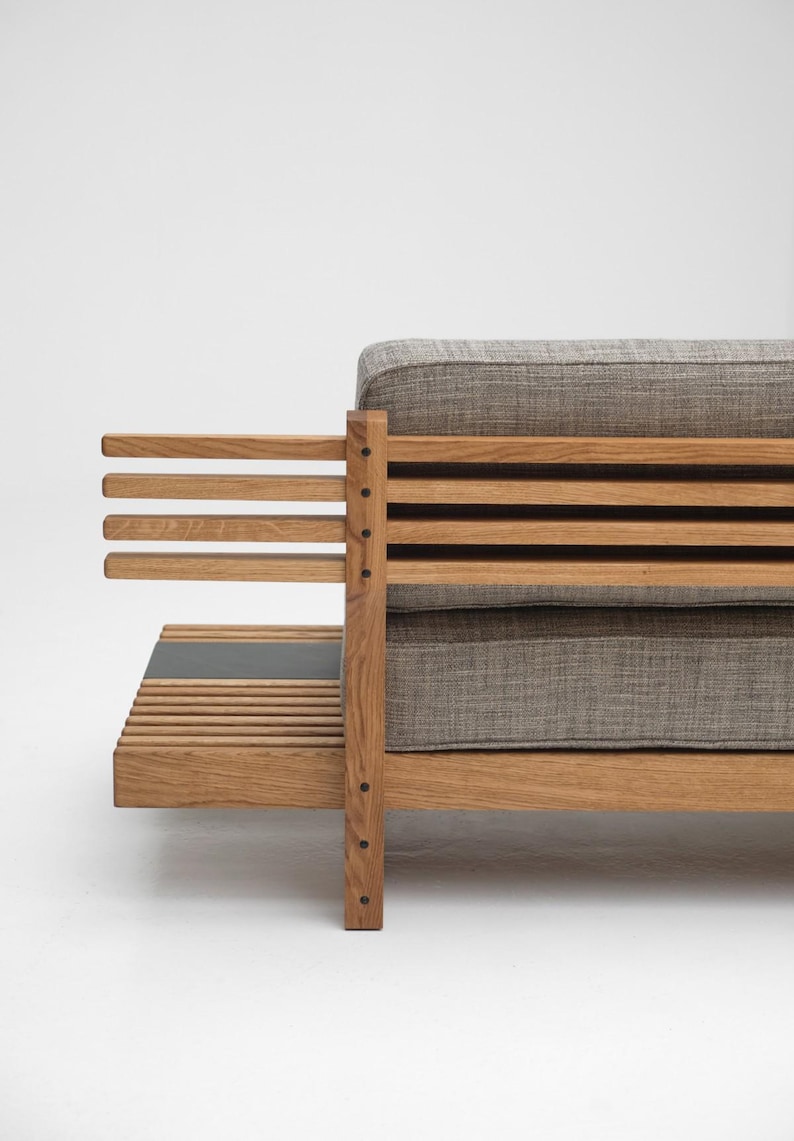 May include: A wooden sofa with a gray fabric cushion and a slatted back and armrests. The sofa has a small shelf underneath the seat.