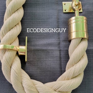May include: A thick, beige rope with gold metal end caps and a loop. The rope is coiled in a circle and the end caps are visible. The background is a dark gray fabric.