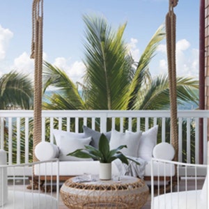 May include: White wicker patio furniture with white cushions and a woven wicker coffee table. The furniture is on a wooden deck with a view of palm trees and the ocean.