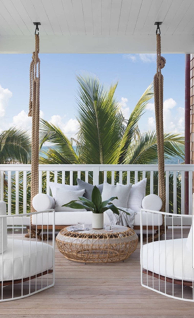 May include: White wicker patio furniture with white cushions and a woven wicker coffee table. The furniture is on a wooden deck with a view of palm trees and the ocean.