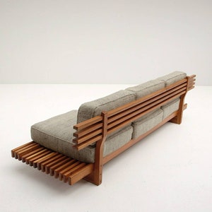 May include: A wooden sofa with a slatted back and a slatted base. The sofa is upholstered in a light gray fabric.