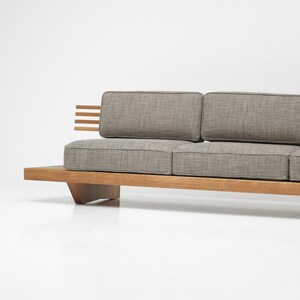 May include: A gray fabric sofa with a wooden frame and a low profile. The sofa has a simple design with a rectangular shape and a slightly angled base.