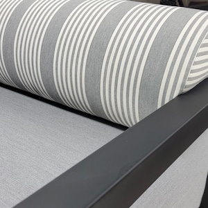 May include: A close-up of a gray and white striped cushion resting on a black metal frame. The cushion is made of a soft, textured fabric.