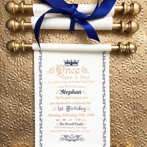Puede incluir: Una invitación en rollo blanco con detalles dorados y una cinta azul. La invitación dice "Érase una vez, en una tierra encantada lejana, vivía un pequeño PRÍNCIPE llamado Stephan. Por su solicitud real, estás invitado a celebrar su 1er cumpleaños el domingo 25 de febrero de 2018 a la 1:00 pm en el Castillo Terrell 8052 Hillandale Dr. San Diego Por favor, confirma tu asistencia con el Rey al 155.3335.321"