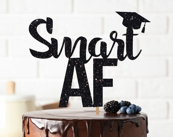 May include: A chocolate cake with chocolate ganache frosting and a black glitter cake topper that says "Smart AF" with a graduation cap on top. The cake is on a white cake stand.