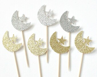 May include: Set of eight gold and silver glitter crescent moon and star cupcake toppers. The toppers are attached to wooden skewers.