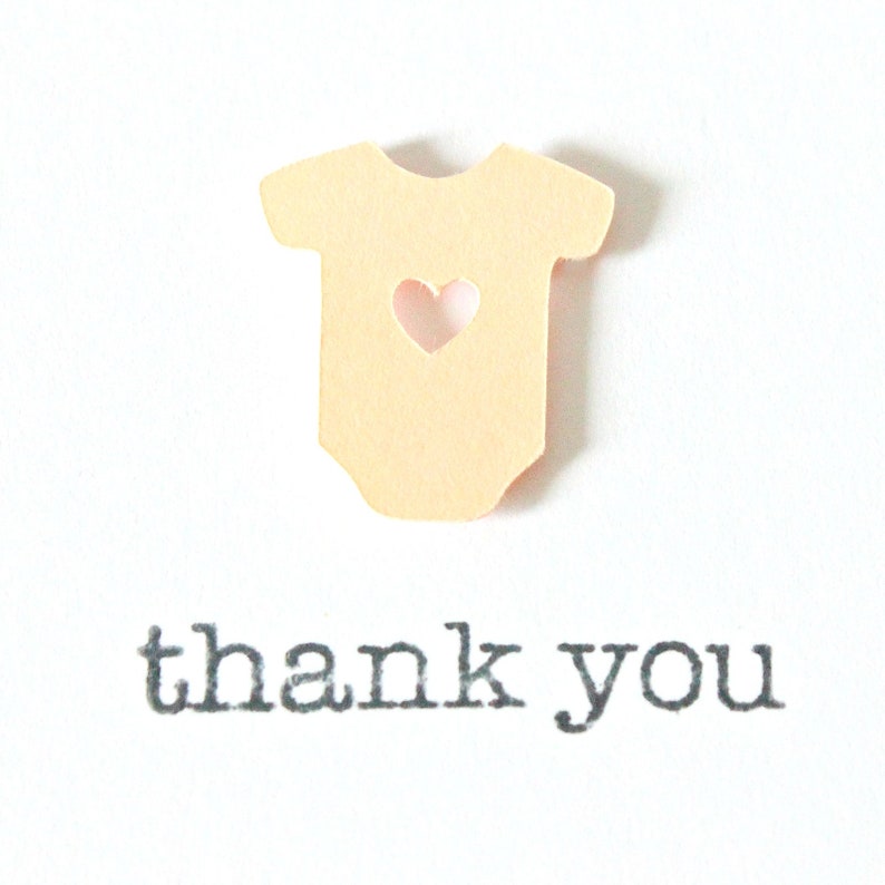 May include: A light yellow paper cutout of a baby onesie with a heart-shaped hole in the center. The text "thank you" is printed below the onesie.