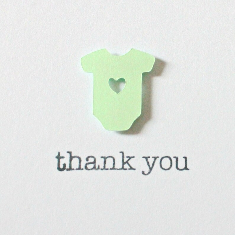 May include: A green paper cutout of a baby onesie with a heart cutout in the center. The text "thank you" is printed below the onesie.