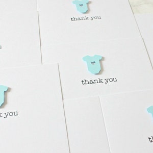 May include: Set of five thank you cards with a light blue baby onesie cutout with a small heart in the center. Each card says "thank you" in black text.