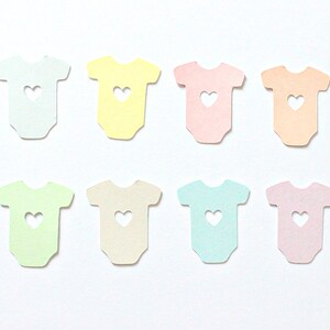 May include: Eight pastel-colored paper cutouts of baby onesies with a heart-shaped hole in the center. The onesies are in shades of blue, green, yellow, pink, and peach.