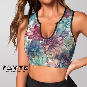 May include: A white sports bra with a floral print of succulents in shades of green, purple, and pink. The bra has a black trim and a keyhole neckline.