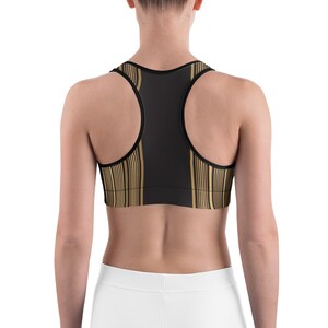 May include: Black sports bra with gold vertical stripe pattern. The bra has a racerback design and is made of a stretchy material. The bra is designed for athletic activities.