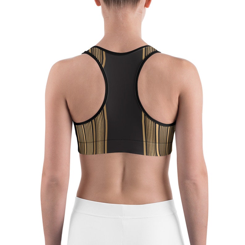 May include: Black sports bra with gold vertical stripe pattern. The bra has a racerback design and is made of a stretchy material. The bra is designed for athletic activities.