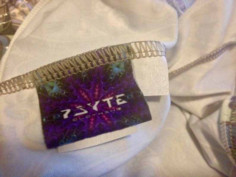 May include: A purple, blue, and green label with the text "PSYCTE CLOTHING" on a white background. The label is attached to a white garment with a brown seam.