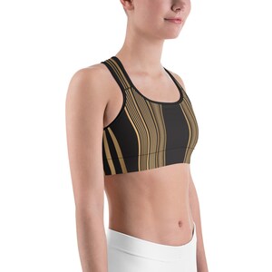 May include: Black sports bra with a gold vertical wavy stripe pattern. The bra has a racerback design and a scoop neckline. The fabric appears to be a soft, stretchy material, suitable for athletic activities.