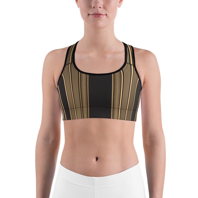 May include: Black and gold striped sports bra with a scoop neck and racerback design. The bra features vertical gold stripes on a black background, with black trim around the neckline and straps. The sports bra is designed for athletic activities.