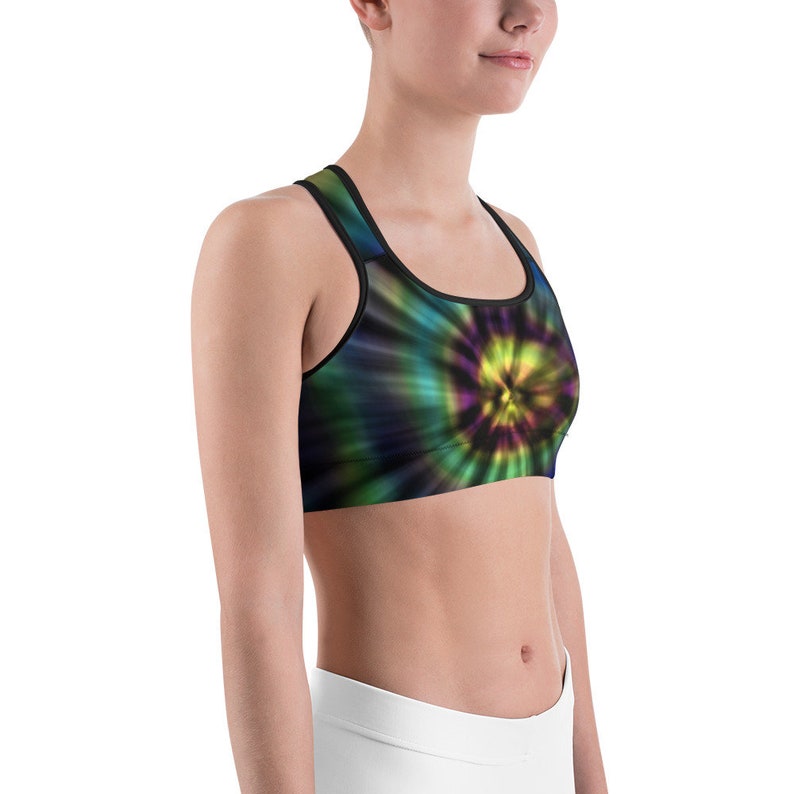 May include: A sports bra with a tie-dye pattern in shades of green, blue, and yellow. The bra has a black trim and a scoop neckline. The tie-dye design radiates from the center.