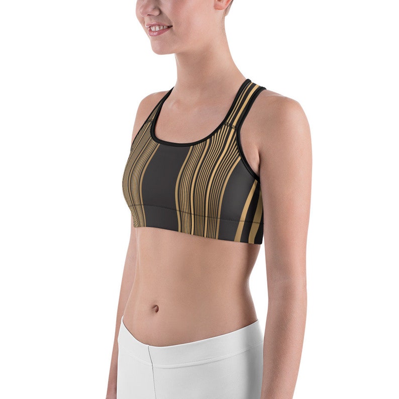 May include: Black and gold striped sports bra. The bra features a black base with vertical gold stripes. The straps and trim are black. The sports bra is designed for athletic activities.