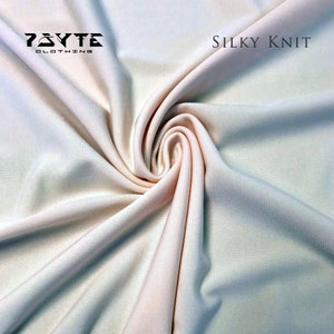 May include: Close-up of a soft, pale pink fabric with a silky knit texture. The fabric is draped and folded, showing its smooth and flowing quality. The text "PSYTE CLOTHING" and "SILKY KNIT" is visible in the top corners of the image.