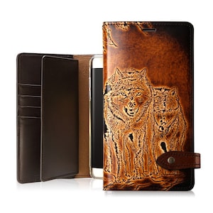 Puede incluir: Una funda de teléfono de cuero marrón con una solapa de cartera y un diseño de dos lobos tallados en el cuero. La funda tiene una ranura para tarjetas de crédito y una correa para mantenerla cerrada.