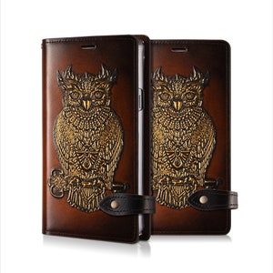 May include: Two brown leather phone cases with a gold embossed owl design. The cases have a black leather strap with a snap closure.