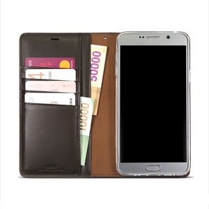 May include: A brown leather phone case with a built-in wallet. The case has slots for credit cards and a pocket for cash. The phone case is open and a smartphone is visible inside.