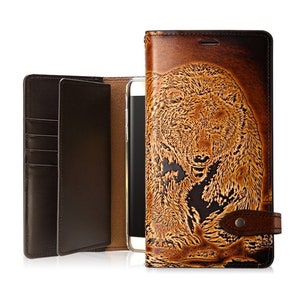 May include: A brown leather phone case with a detailed embossed image of a bear. The case has a flap that folds over the phone and a slot for credit cards.