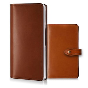 May include: Two brown leather covers for notebooks or planners. The taller cover on the left is rectangular with rounded corners. The shorter cover on the right features a horizontal strap with a metallic snap button closure and matching stitching.