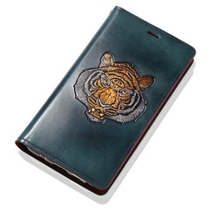 May include: A teal leather phone case with an embroidered tiger face in gold and silver.