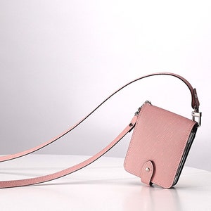May include: A pink leather wallet with a long strap. The wallet has a flap closure and a silver buckle.