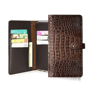 May include: A brown leather wallet with a crocodile skin texture. The wallet is open, showing multiple card slots filled with cards and a banknote. The wallet is closed with a snap closure.
