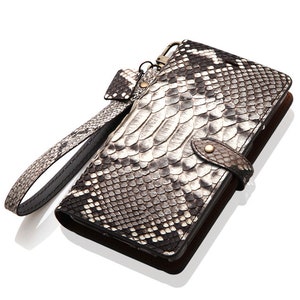 May include: A black and white snakeskin leather wallet with a wrist strap. The wallet has a flap closure and a metal clasp.